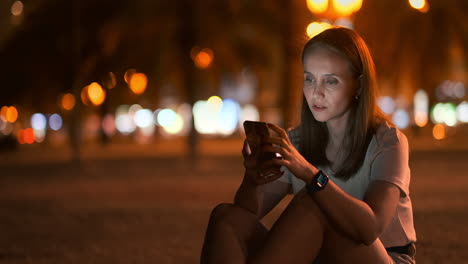 Young-woman-tourist-travels-through-the-night-megalopolis-and-writes-text-messages-on-social-networks-about-the-journey-holds-the-phone-in-her-hands-and-looks-at-the-screen-of-the-gadget